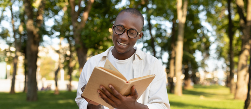 A young person holding a journal in a field of trees practices mental health journaling. 