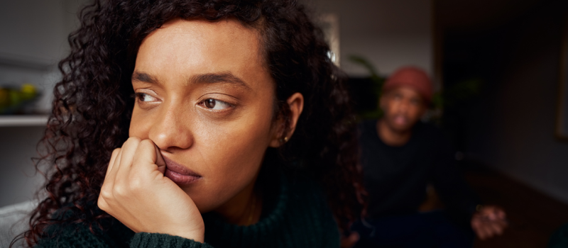 A person dealing with complex PTSD triggers in her relationship looks into the distance while her partner sits in the background.