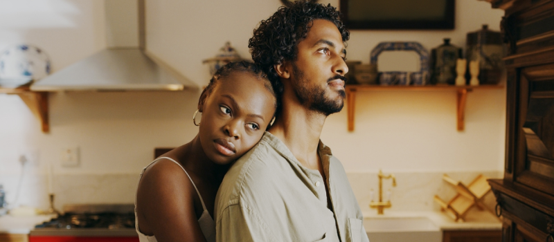 A couple embraces in a kitchen. One partner, who has persistent anxiety, is wearing a tank top and the other is wearing a collared shirt.