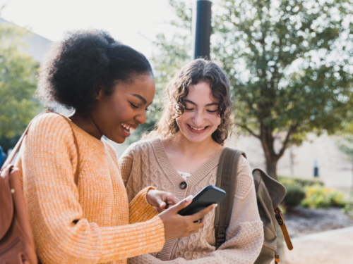 Two young people smile while looking at a phone as they watch TikTok videos of beige flags.