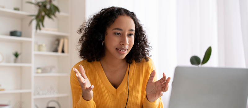 Female in orange sweater sitting at a table in virtual therapy where she is discussing with her therapists goals she has for therapy.