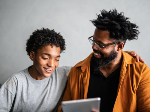 A father and son look at a screen where they are reading about life skills for teens.