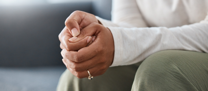 Person sitting on couch with white shirt and green pants on. The individual is stimming through touch by picking at their nails.