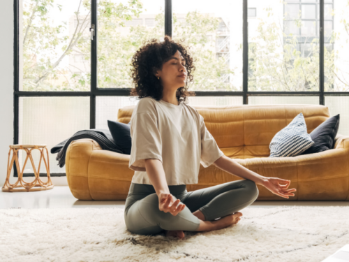 A woman with PTSD meditates on the floor with her legs crossed practicing a PTSD symptom management meditation.