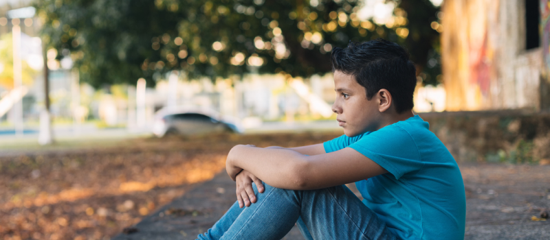 A young person dealing with intermittent explosive disorder sits on the ground in a blue shirt and jeans.