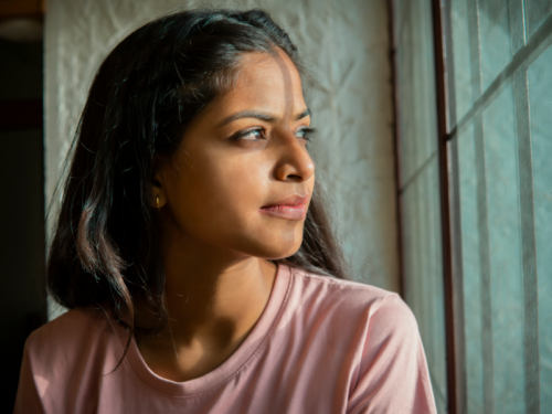 Woman in pink shirt looking out of her window. She was diagnosed with a mental illness and is in treatment.