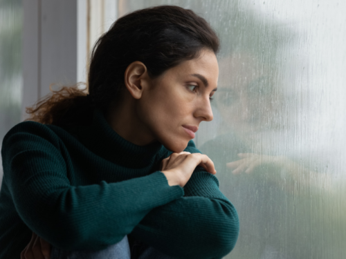 A woman in a green shirt dealing with anxiety-induced dizziness looks out the window to calm herself.