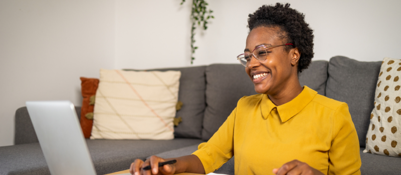 A person who is questioning their gender identity smiles at a computer screen during an affirming gender therapy session.