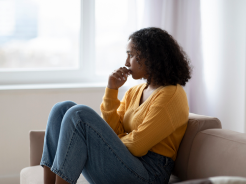 Woman in an orange sweater sitting on a couch. She is being treated for anxiety and suicidal ideation.