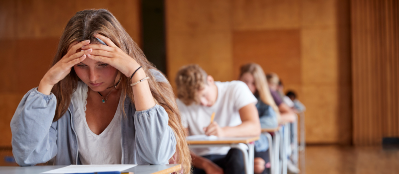 A young woman in a blue zip-up dealing with anxiety-induced dizziness during an exam puts her hands on her head to ease her anxiety.