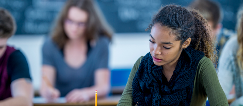 A person in a green sweater sits at a desk holding a pencil. She is able to manage school work and severe OCD with the help of therapy and medication.