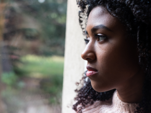 A young woman looks out of the window in her home. She is in somatic therapy to address the somatic memories she is having.