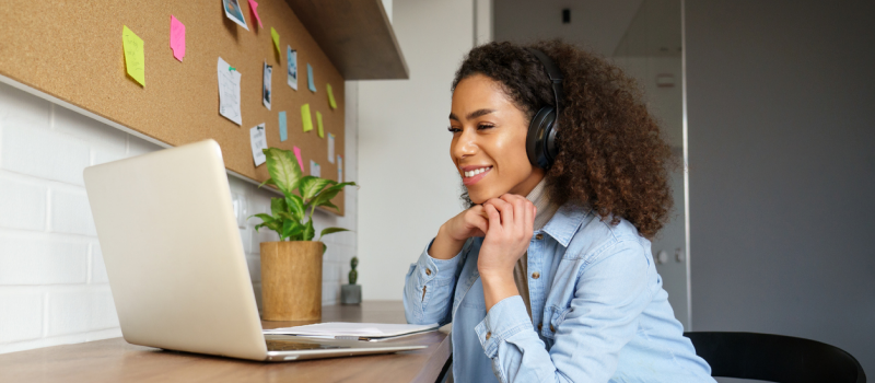 Young female in a denim jacket wearing black headphones. She is sitting at a table in virtual intensive outpatient programming.