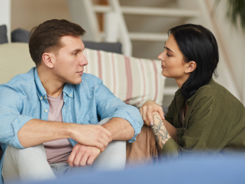 A young woman in a green shirt sits with her partner in a blue shirt. She has anxiety and they are discussing the ways in which he can best support her.