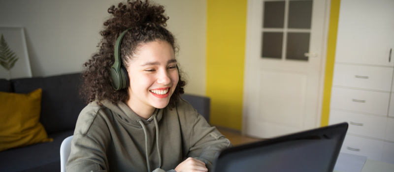 Female teenager in a green sweatshirt and headphones in her room. She is in virtual Intensive Outpatient Programming, learning somatic exercises to improve her mental health.