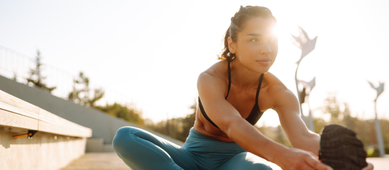 A young woman stretches outside. She recently learned what somatic stretching is and is putting it into practice.