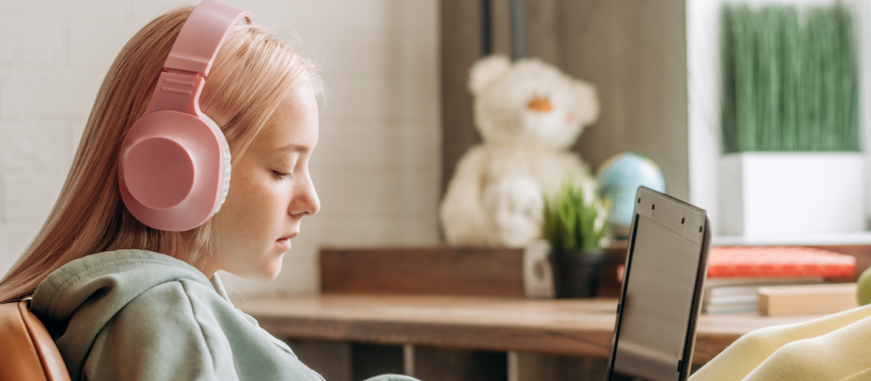 A teenager in a green sweatshirt with headphones and her computer. She is a suicide attempt survivor receiving support through Charlie Health's vIOP.