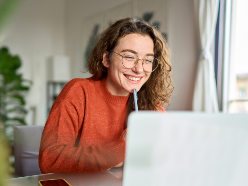 A young female in a red shirt sits at her desk on her computer. She is in Charlie Health's vIOP and her engagement data can help personalize her care.