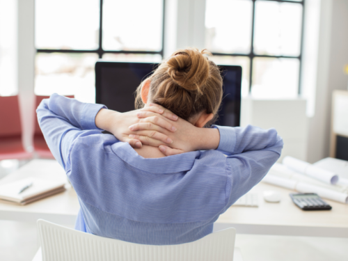 A woman in a light blue shirt faces her computer at her desk. She is reading about somatic stretching.