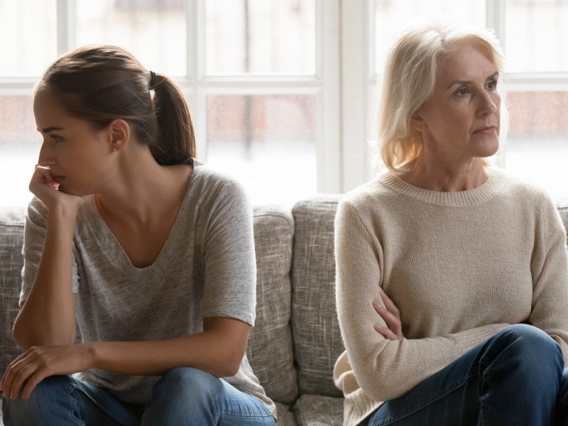 A mother and daughter sit on a couch looking away from each other; the mother has her arms crossed and the daughter is resting her head on her hand. The two face challenges in their relationship since the mother has narcissistic personality disorder (NPD).