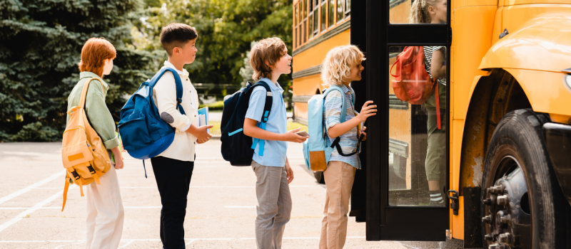 A group of students, who are returning back-to-school, line up in front of a yellow school bus for the first day of class. They are feeling a range of mental health symptoms—from excited to nervous—about returning to school.