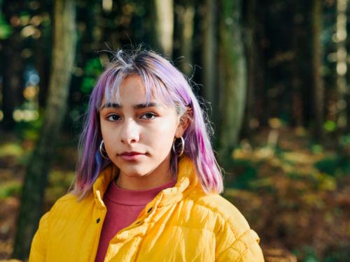 A young female in a yellow jacket. She is on a walk in the woods.