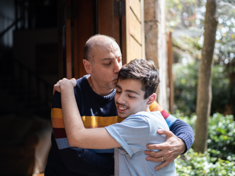 A father hugs his teen son. His son is in therapy for depression.
