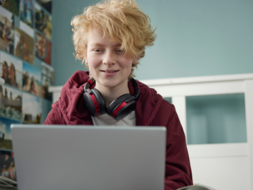 A teenager in a red sweatshirt and grey shirt sits on their bed. They are on their computer reading about what it means to be gender apathetic.