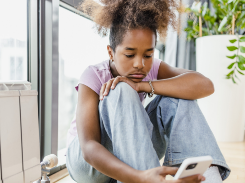 A young female in a pink shirt and jeans on her phone. She intellectualizes instead of feeling her feelings.