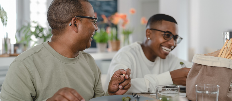 Two brothers sit next to each other at the dinner table. One of them is practicing the PLEASE DBT Skill and eating balanced meals.