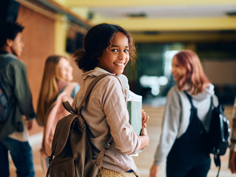 A young female walks with friends in her high school hallways. She knows mental health tips for high school students.