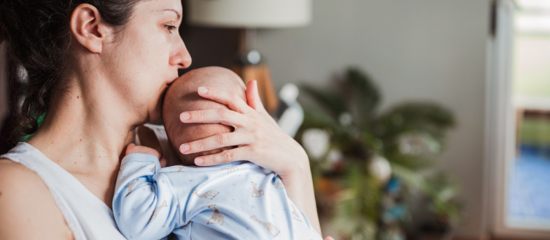 A new mom who is dealing with new mom anxiety, also known as postpartum anxiety, holds her baby and feels worried about its safety.