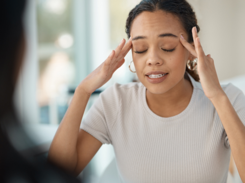 A new mother in a white shirt sits in a therapy session with her hands on her temples as she talks about her postpartum OCD symptoms.