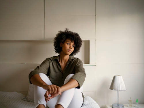 A person in a green long sleeve shirt sits on a bed looking into the distance after an argument with her friend who is a narcissist.