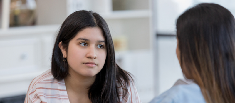 A teenager sits with her younger sister. She is experiencing oldest daughter syndrome.