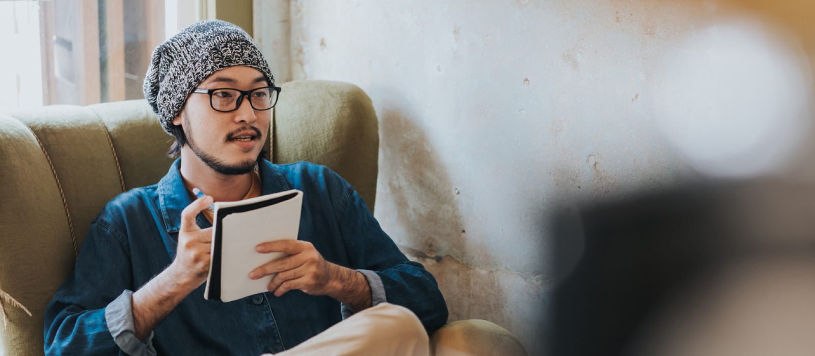 A young male sits at home in his living room with his journal. He is using CBT journal prompts.