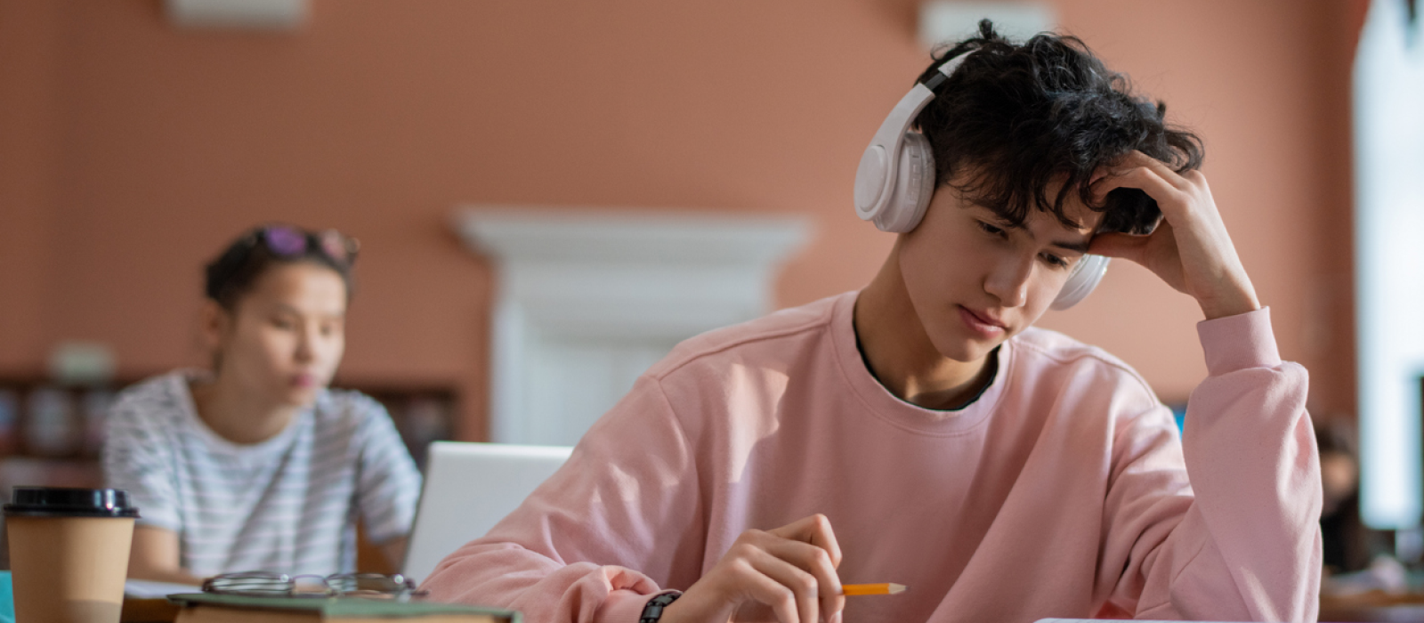 A male teenager sits in class doing work. he is having ADHD burnout.