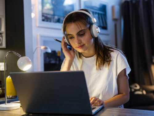 A female teenager in a white shirt and headphones. She is on her computer researching what the best therapy for depression is.