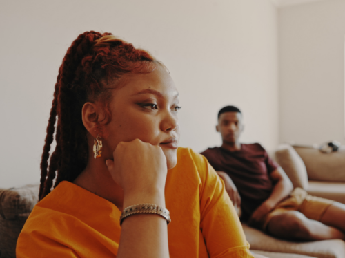 A young woman sits on the couch, away from her boyfriend. She is in an abusive relationship and is feeling like it is so hard to leave.