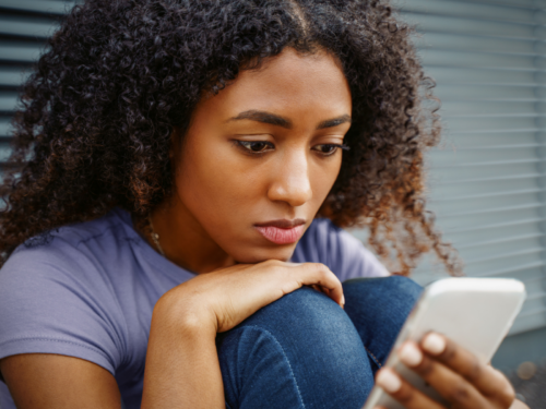 A female teenager sits on the ground on her phone. She has been feeling down and thinks she may have subtle signs of depression.