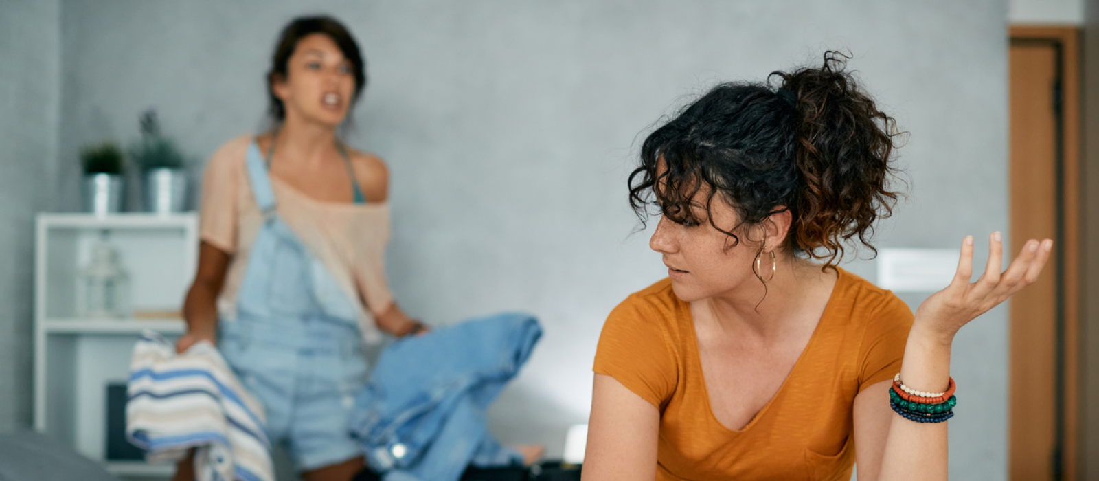 A young woman sits on her bed arguing with her partner, who is folding clothes. She is looking for a therapy that will actually help her heal from narcissistic abuse.