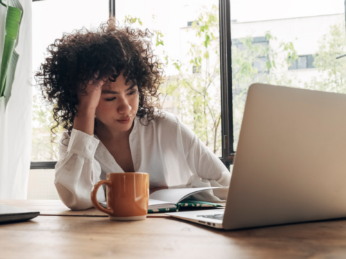 A young woman sits at home on her computer. She is going to do 5 therapist-approved tips for recovering from burnout.