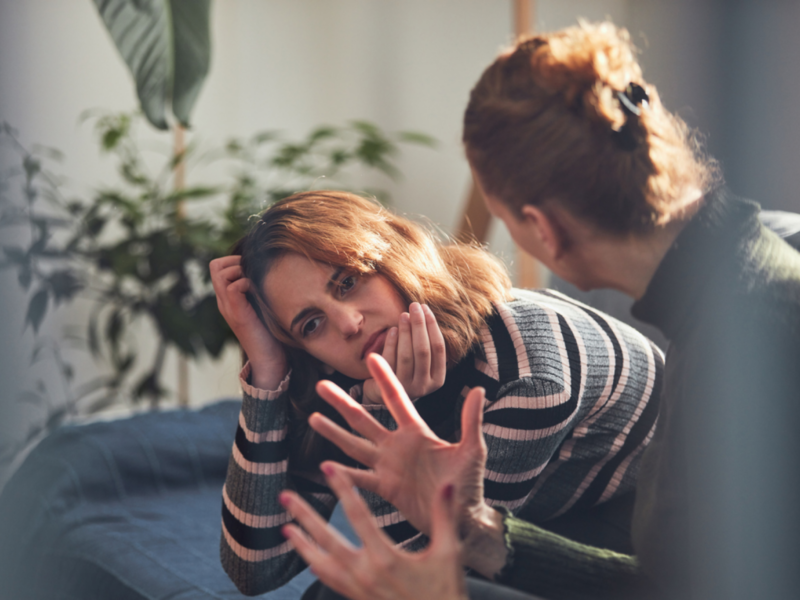 A female teenager sits at home on the couch. Her mother is yelling at her, and she has PTSD from narcissistic abuse.