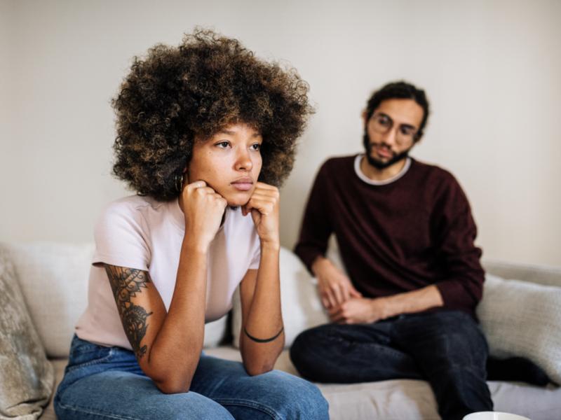 A young woman sits on her couch visibly upset. Her partner is sitting with her. She is in need of therapy that will actually help her heal from narcissistic abuse.
