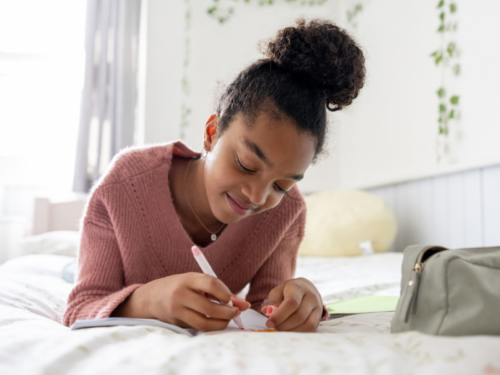 A young girl lays on her bed journaling about using the IMPROVE DBT skill to manage big feelings.