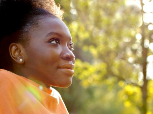 A young female stands outside and enjoys the fresh air. She recognizes this as a glimmer, which can benefit her mental health.