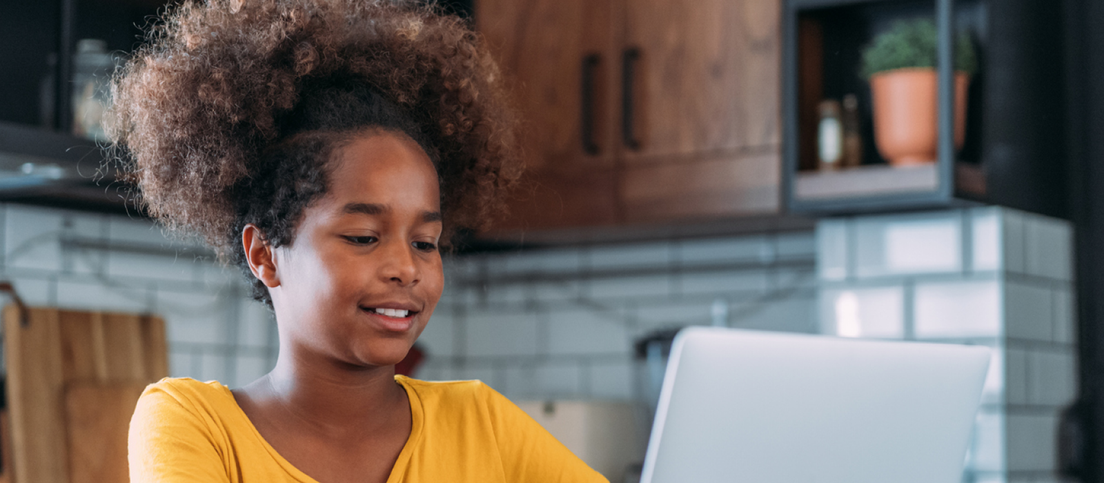 A young girl in an orange shirt sits at home on her computer. She has OCD, and is trying to get the most out of OCD therapy as a young person.