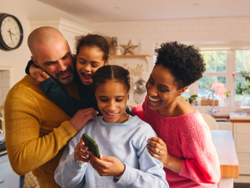 A family crowds around their daughters phone. She is the oldest daughter and is showing them what oldest daughter syndrome is.