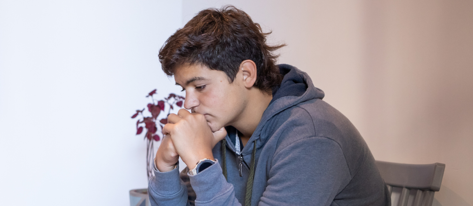 A male teenager sits in a chair in a grey sweatshirt. He is visibly upset, and is looking for the best therapy for depression.