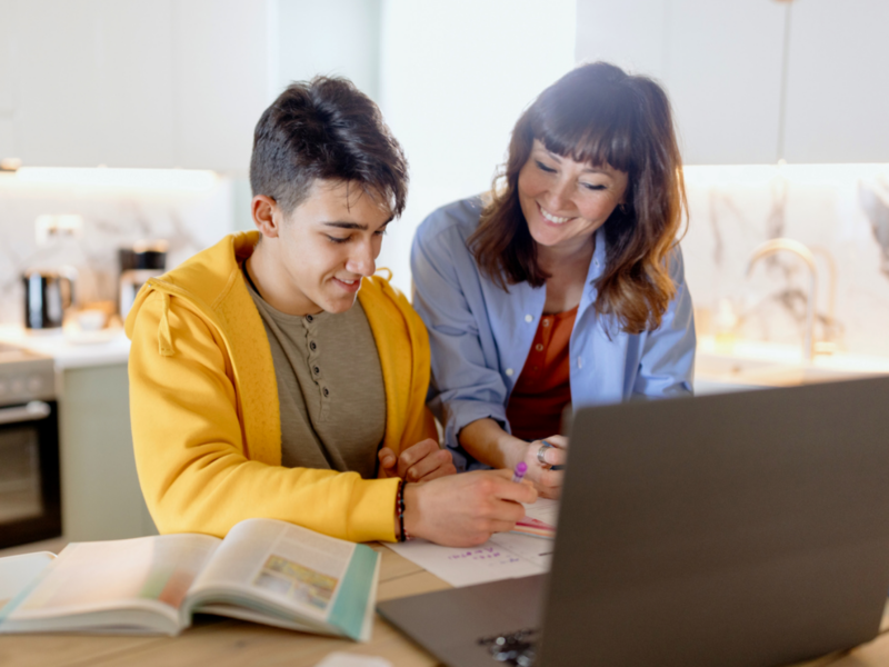 A teenager sits with his mom at their kitchen table. He is in Charlie Health's virtual IOP and has seen an improvement in his physical and mental health.